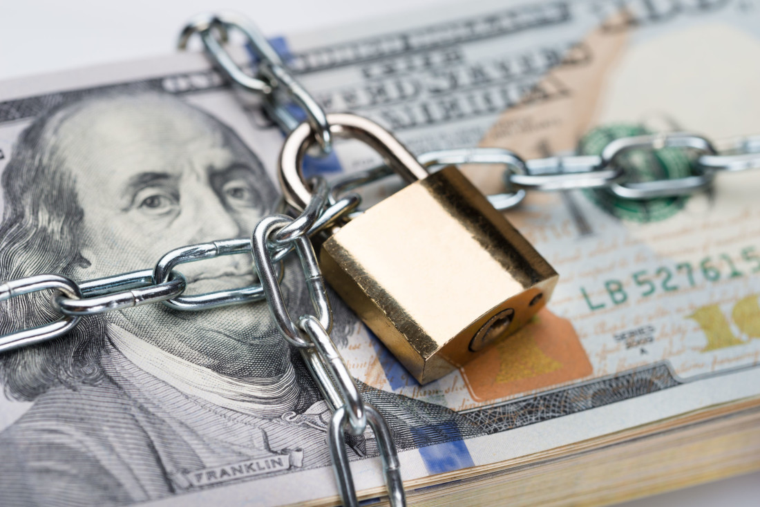 Closeup of metallic chain and padlock around dollar bundle