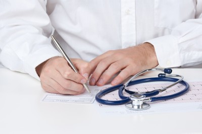Doctor writing on paper with stethoscope on table